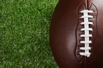 Photo of American football ball on green grass, top view. Space for text