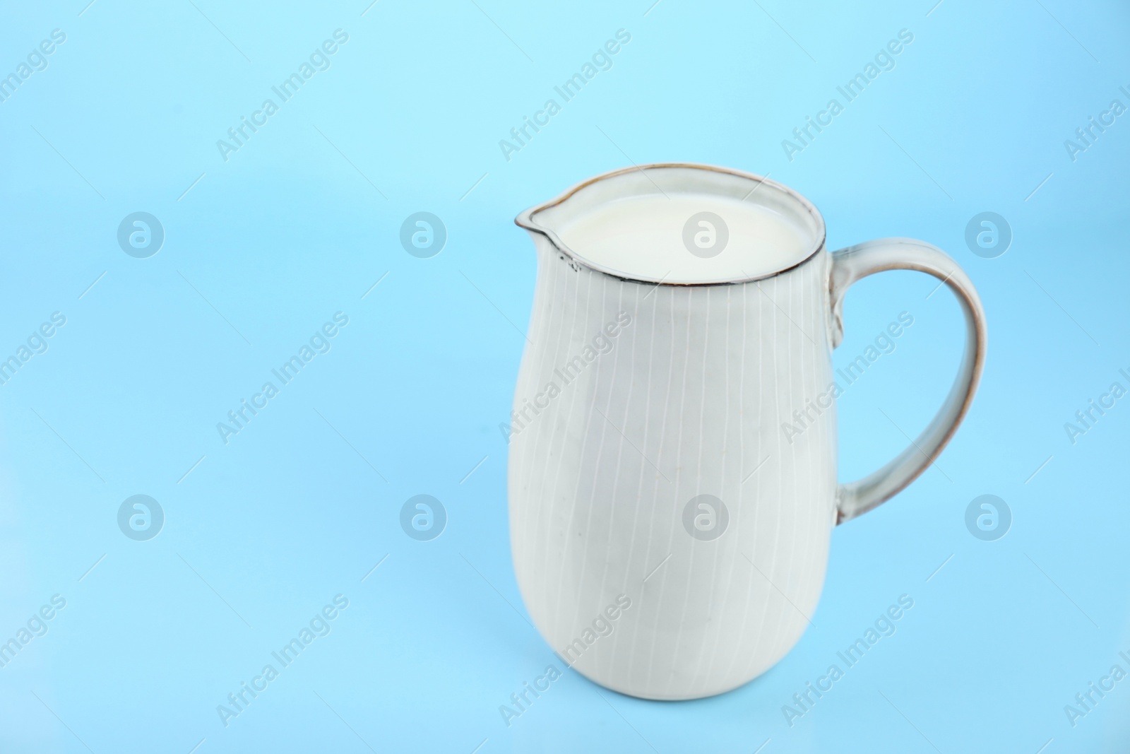 Photo of Jug of fresh milk on light blue background, space for text