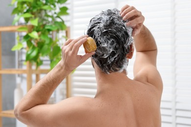 Man washing his hair with solid shampoo bar in bathroom, back view