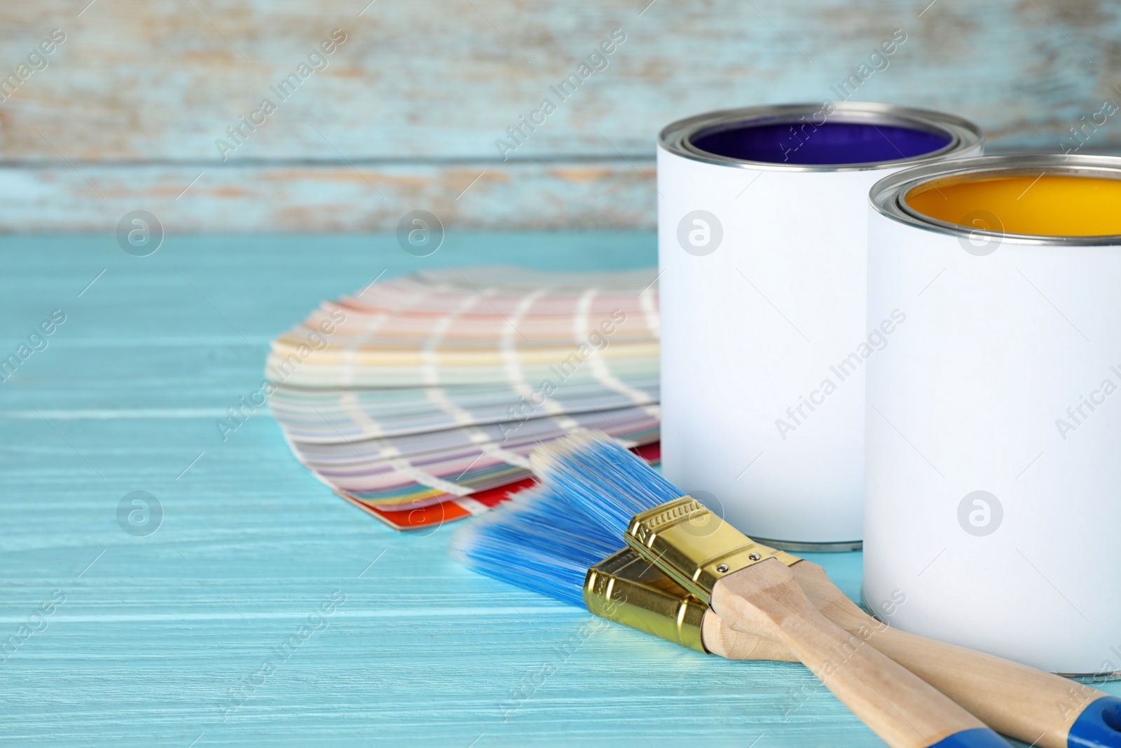 Photo of Cans of paint, brushes and color palette samples on blue wooden table. Space for text