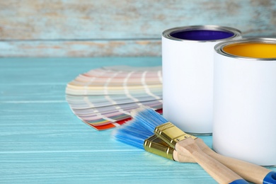 Cans of paint, brushes and color palette samples on blue wooden table. Space for text