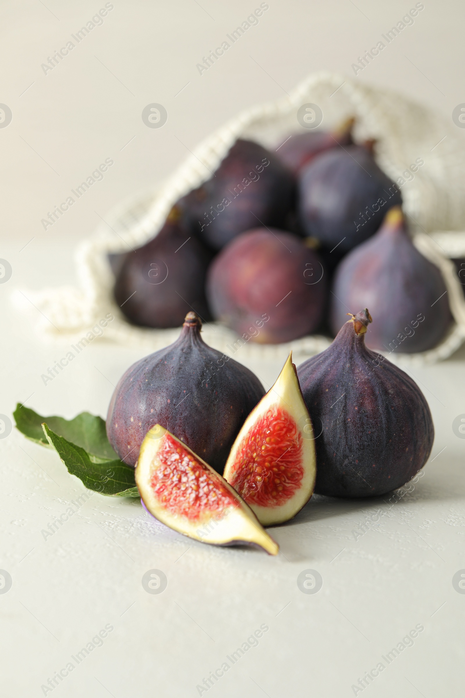 Photo of Whole and cut tasty fresh figs with green leaf on white table