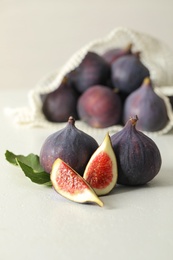 Whole and cut tasty fresh figs with green leaf on white table
