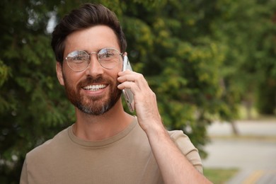 Photo of Smiling bearded man talking on phone outdoors. Space for text