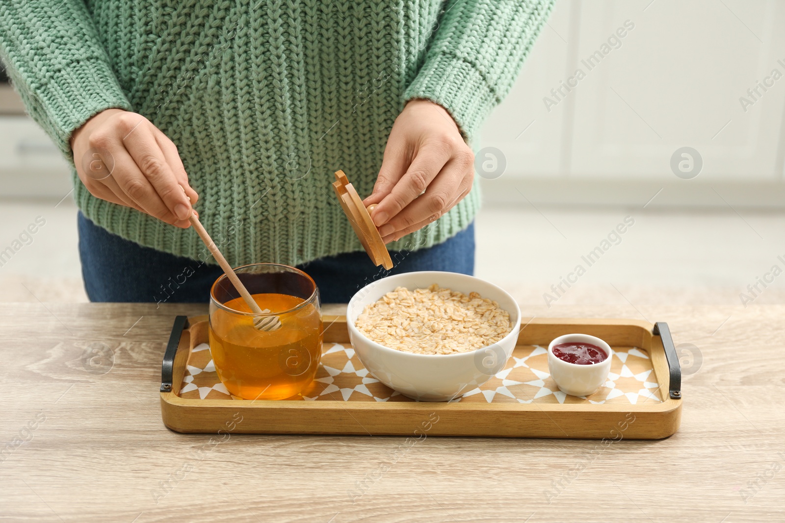 Photo of Woman adding honey to oatmeal at wooden table indoors, closeup