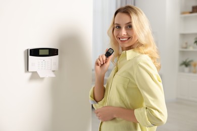 Photo of Home security system. Smiling woman with alarm key fob in room