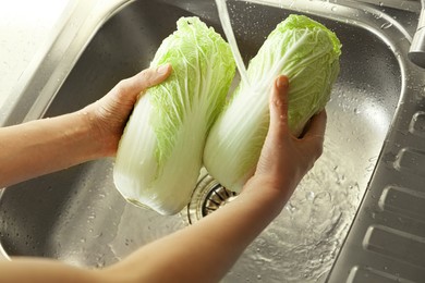 Photo of Woman washing fresh Chinese cabbages in sink, closeup