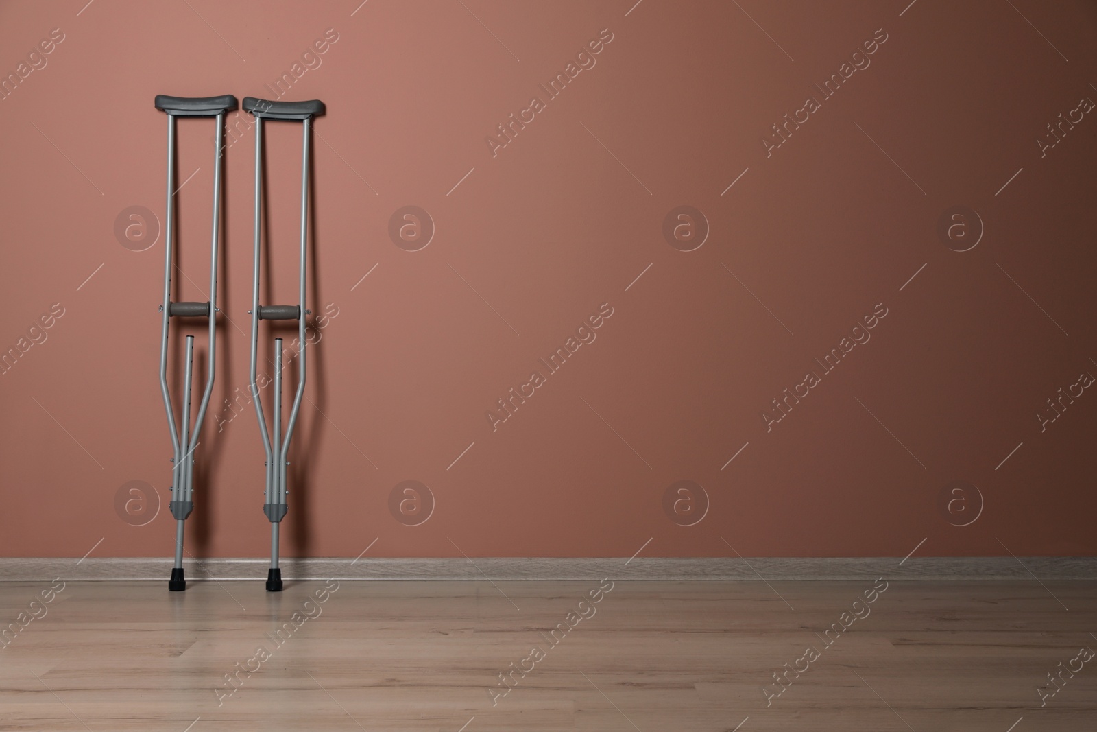 Photo of Pair of axillary crutches near pale pink wall. Space for text