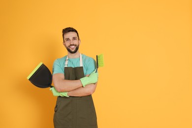 Man with brush and dustpan on orange background, space for text