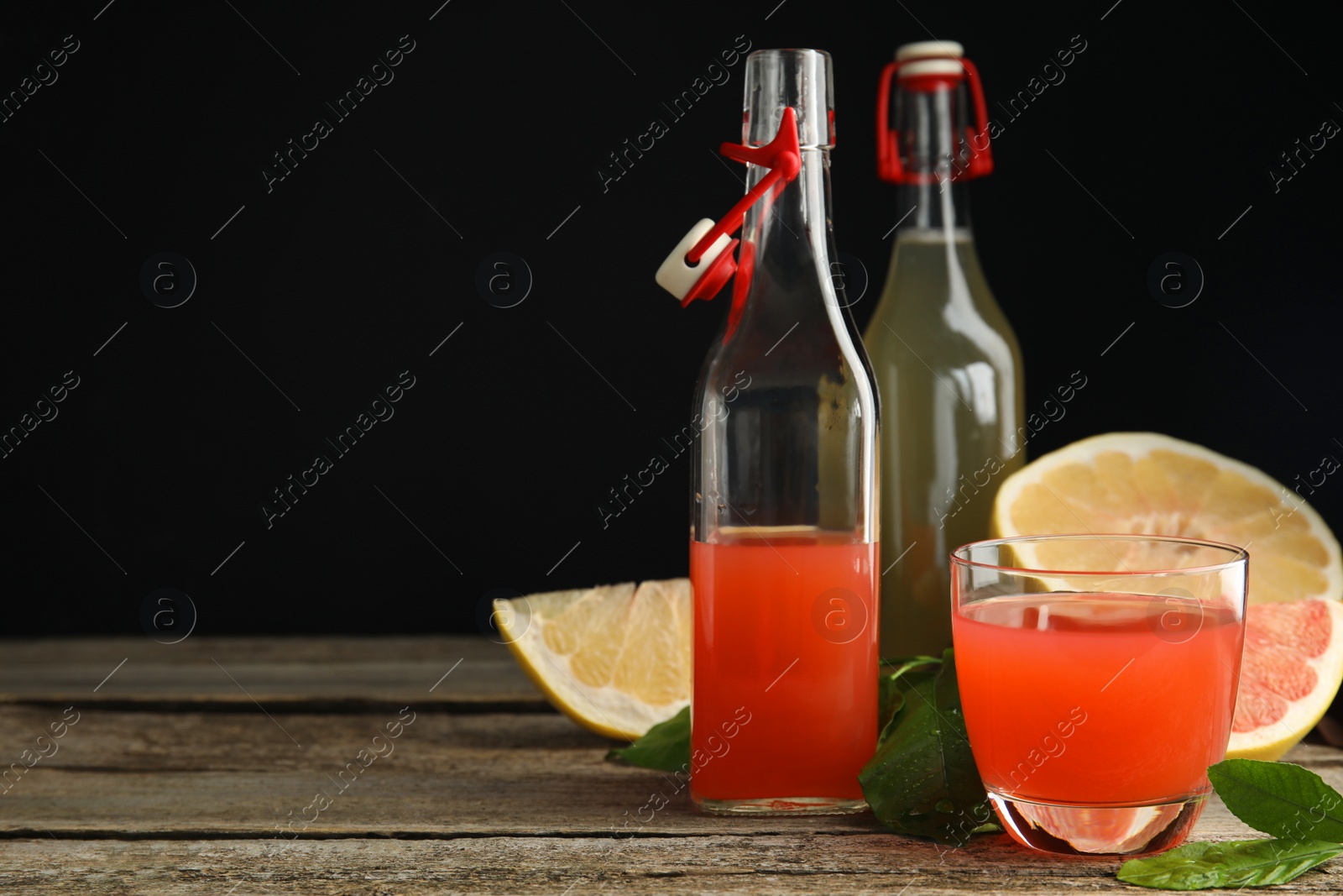 Photo of Glassware of different pomelo juices and fruits on wooden table against black background. Space for text