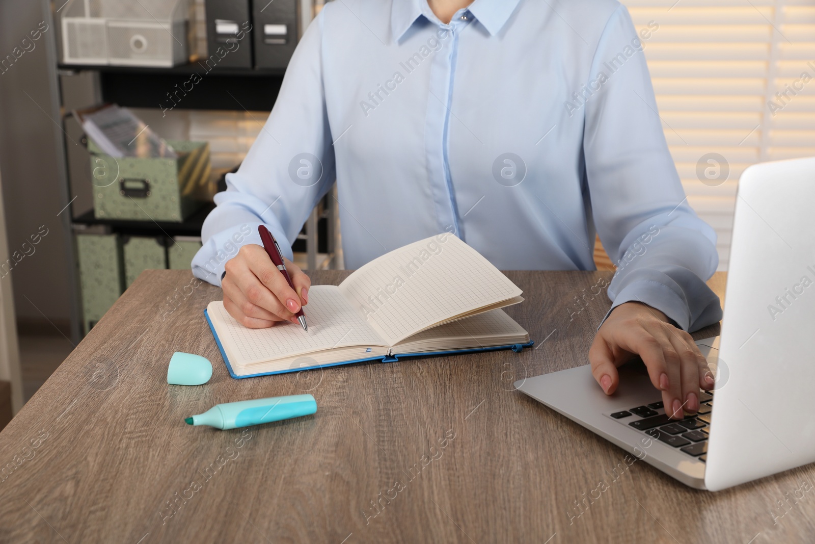 Photo of Woman taking notes while using laptop at wooden table indoors, closeup