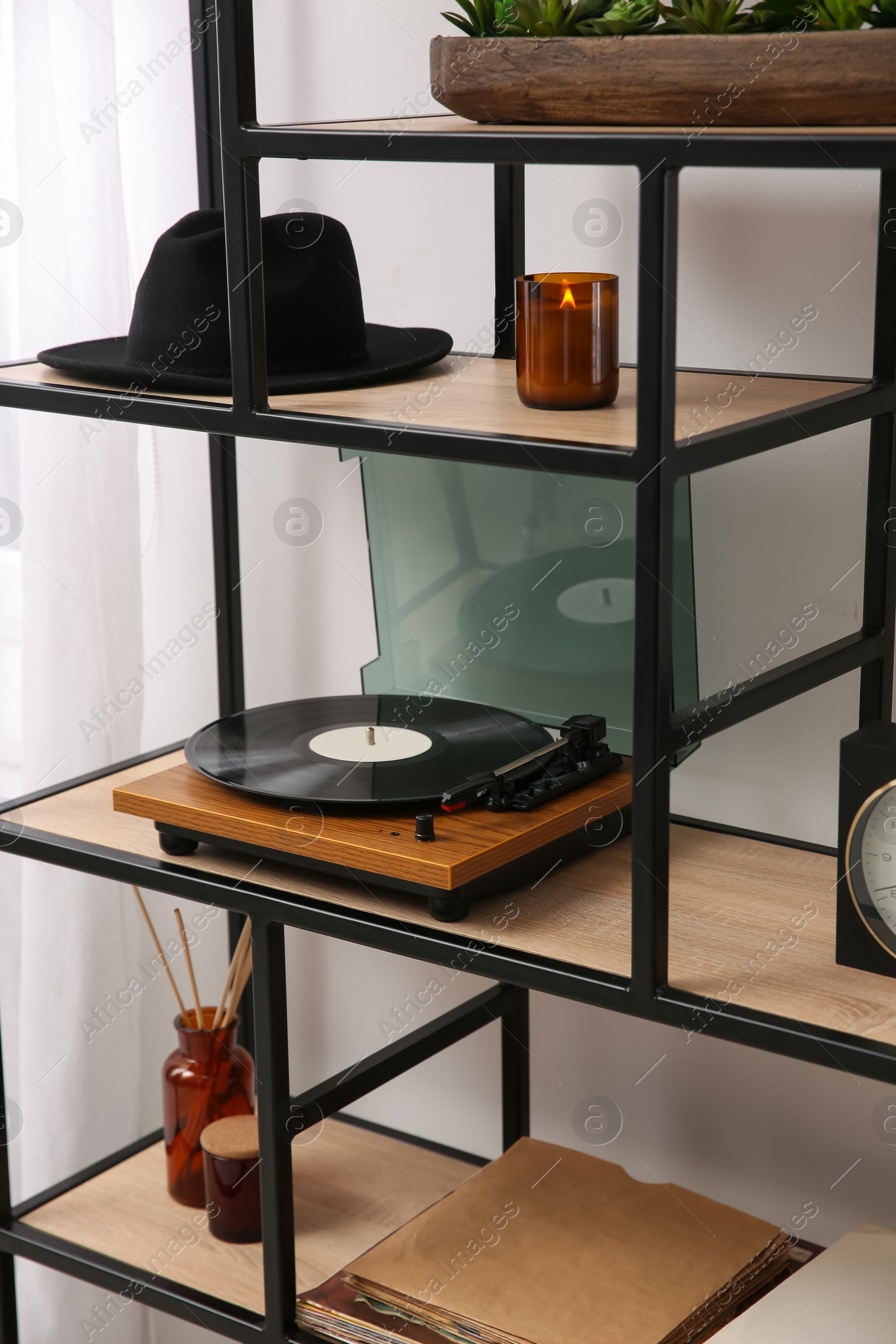 Photo of Stylish turntable with vinyl record on shelving unit indoors