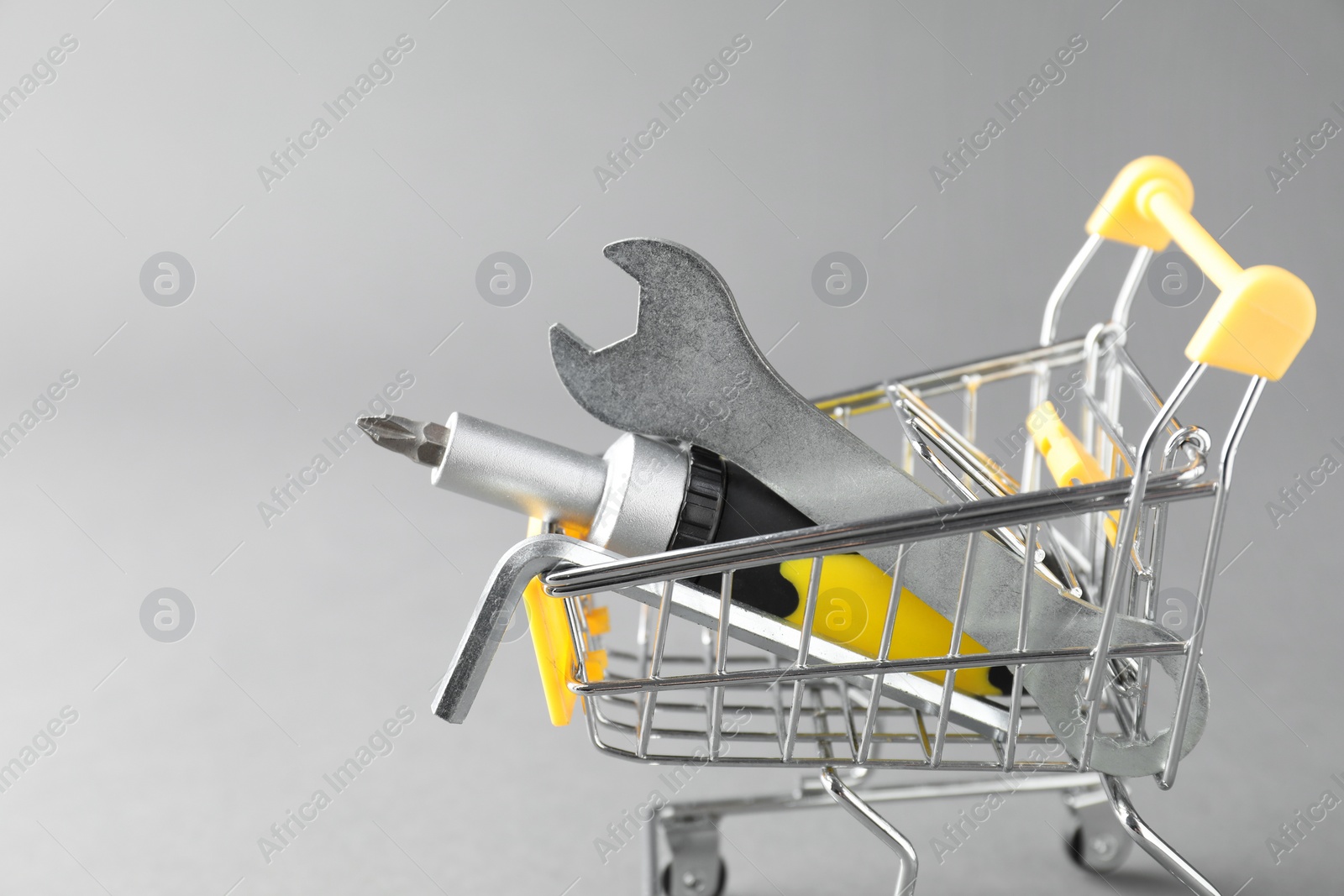 Photo of Small shopping cart with set of construction tools on grey background. Space for text