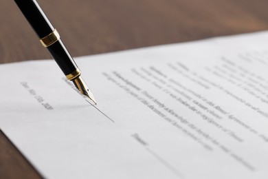 Photo of Writing on document with fountain pen at wooden table, closeup. Notary contract