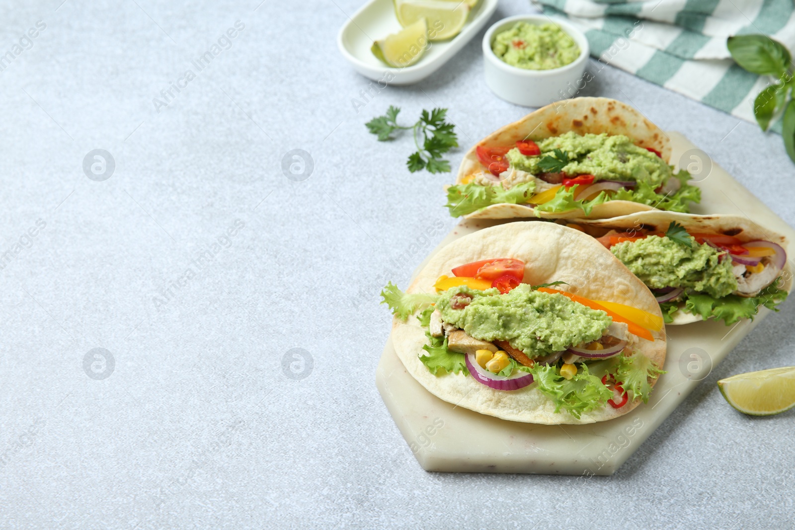 Photo of Delicious tacos with guacamole, meat and vegetables on light grey table, space for text