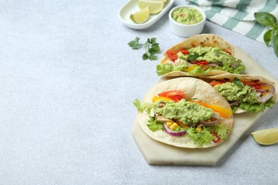 Photo of Delicious tacos with guacamole, meat and vegetables on light grey table, space for text