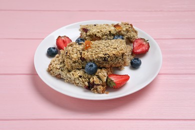 Photo of Tasty granola bars and berries on pink wooden table
