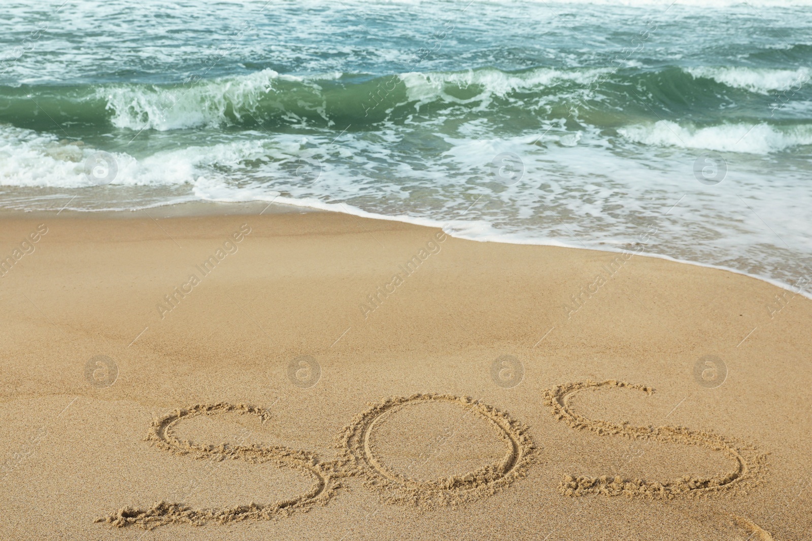 Photo of Message SOS drawn on sand near wavy sea