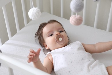 Cute little baby lying in crib with hanging mobile