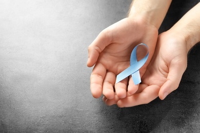 Man holding blue ribbon on grey background, top view. Cancer awareness