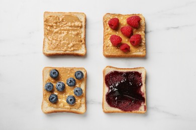 Photo of Delicious toasts with peanut butter, jam, raspberries and blueberries on white marble table, flat lay