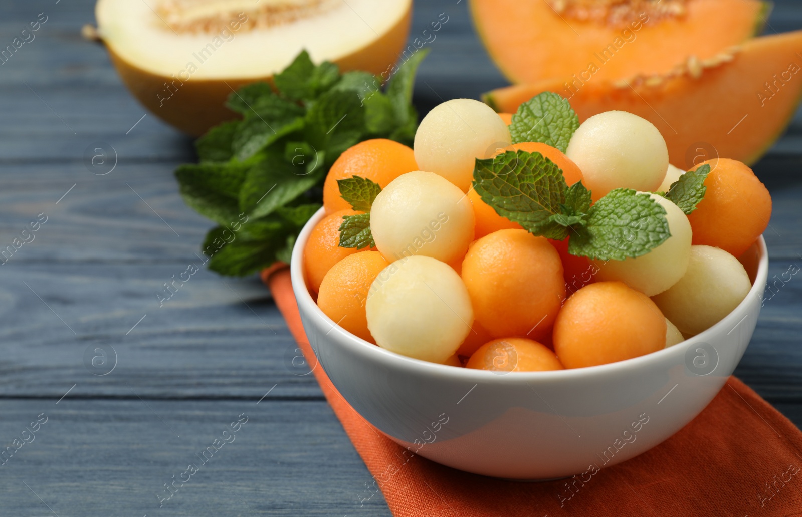 Photo of Melon balls and mint in bowl on blue wooden table, closeup. Space for text