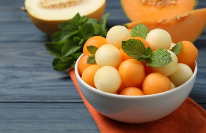 Photo of Melon balls and mint in bowl on blue wooden table, closeup. Space for text