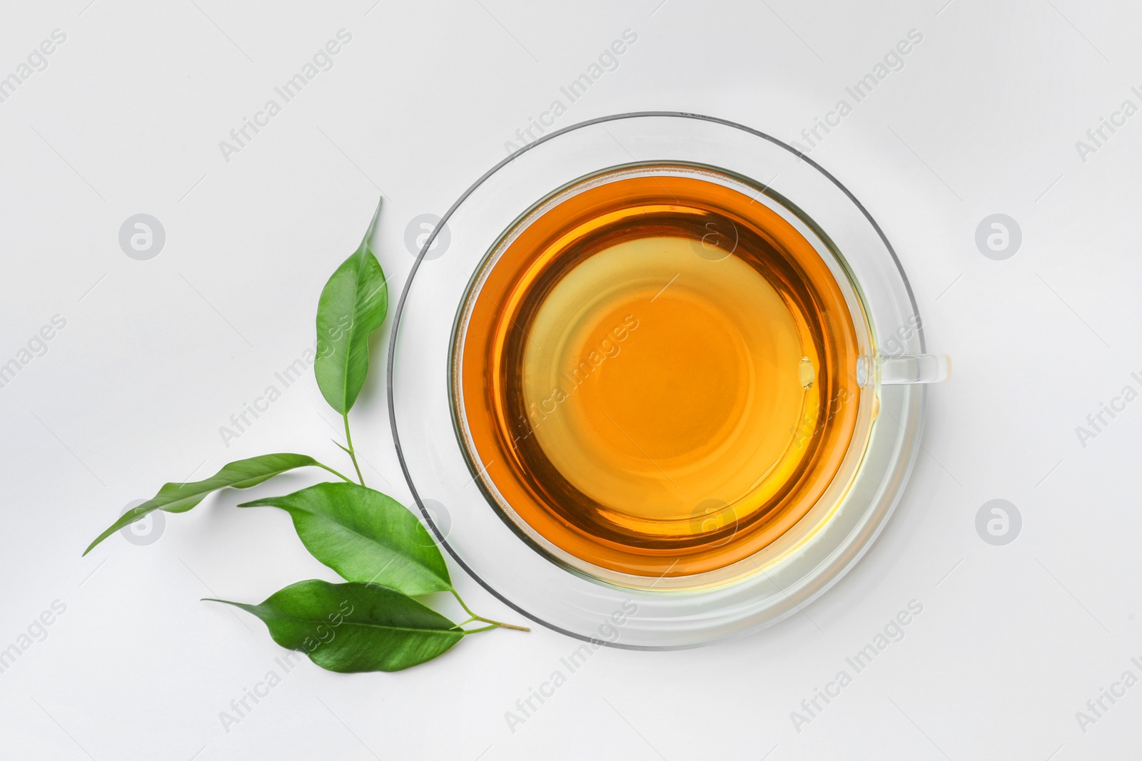 Photo of Fresh green tea in glass cup with saucer and leaves on white table, flat lay