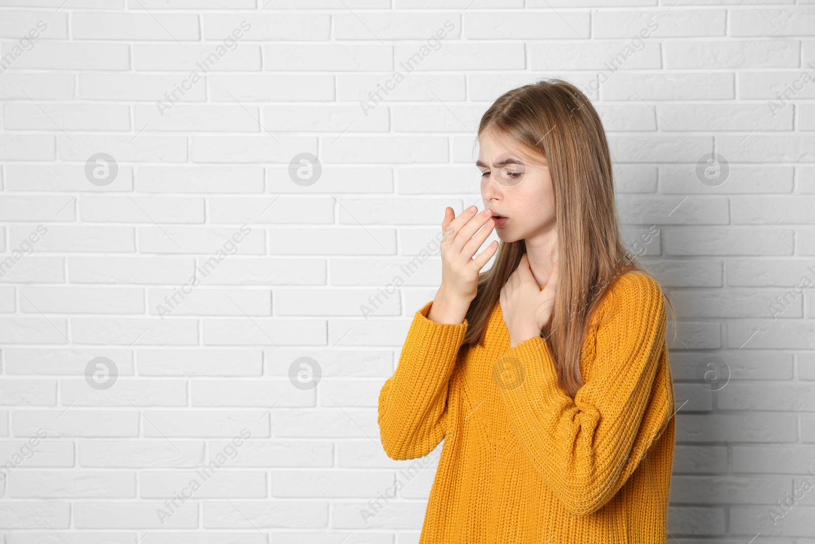 Photo of Teenage girl suffering from cough near brick wall. Space for text