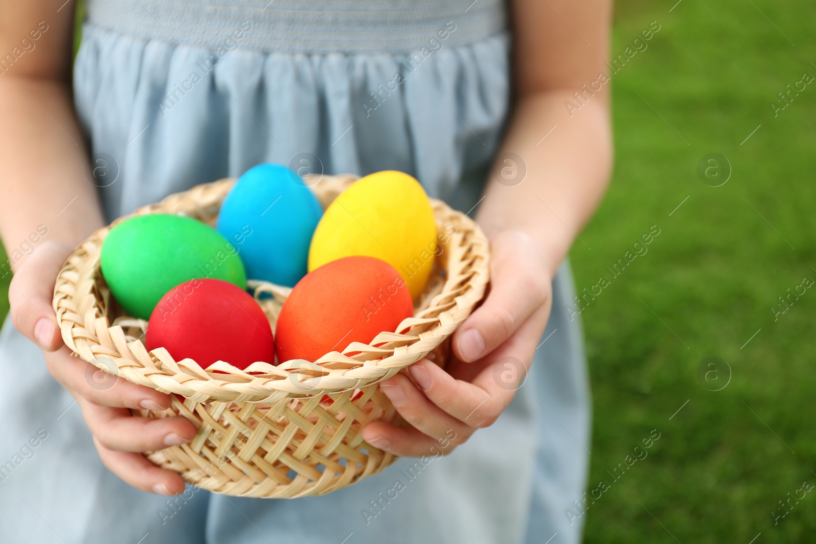 Photo of Cute little girl with basket full of Easter eggs outdoors, closeup