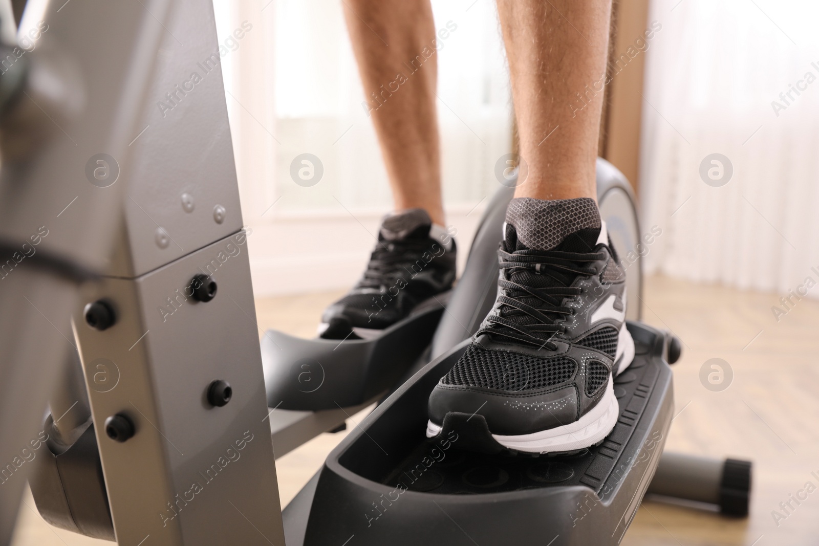 Photo of Man using modern elliptical machine indoors, closeup