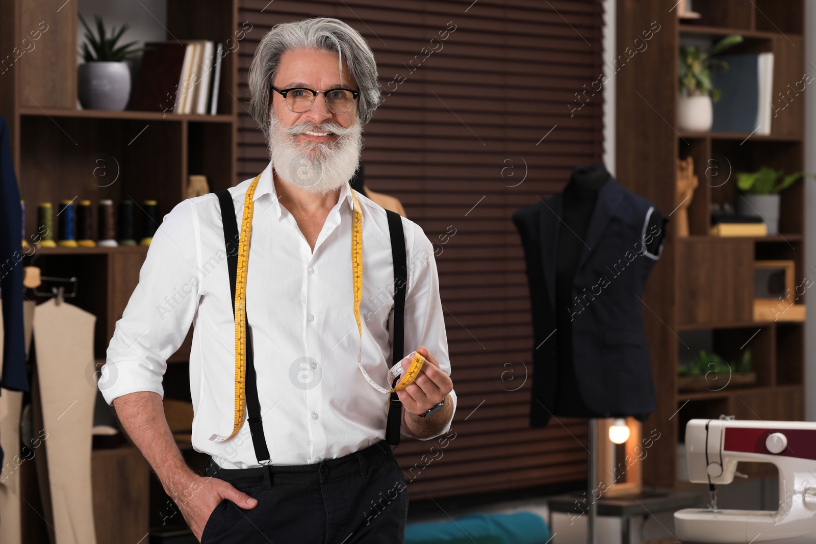 Photo of Professional tailor with measuring tape in workshop, space for text