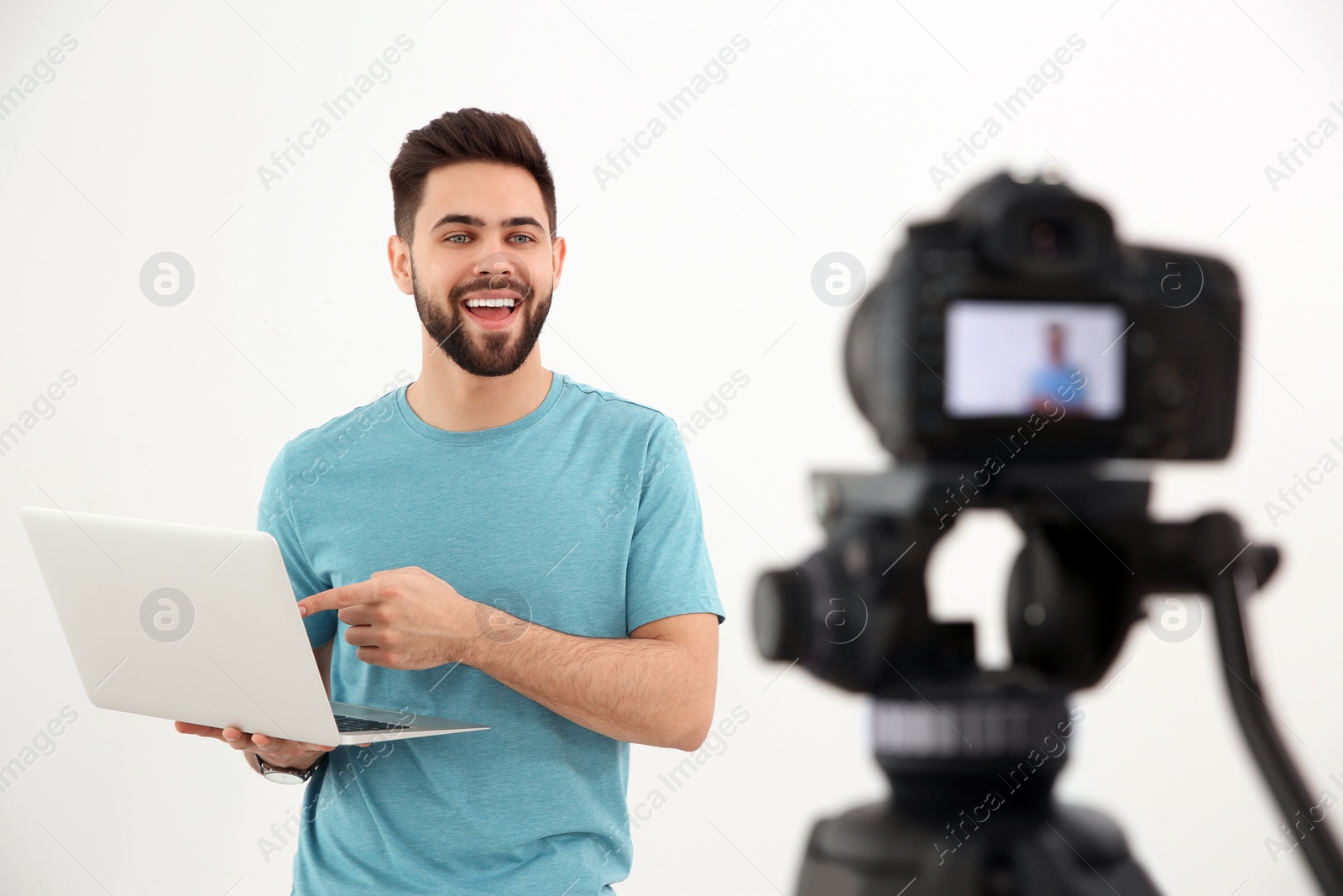 Photo of Young blogger with laptop recording video on camera against white background