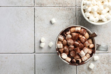 Photo of Delicious hot chocolate with marshmallows, cocoa powder and spoon in cup on tiled table, flat lay. Space for text