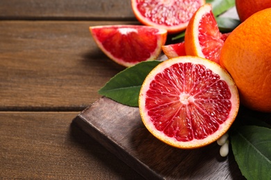 Photo of Cut ripe red oranges and green leaves on wooden table, closeup. Space for text