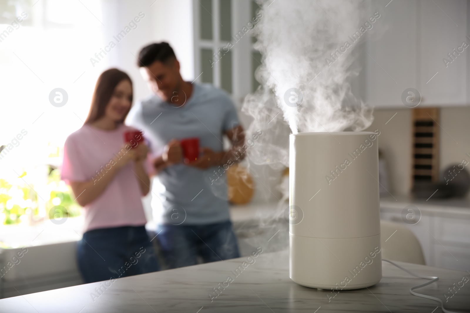 Photo of Modern air humidifier and blurred couple in kitchen