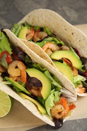 Photo of Delicious tacos with shrimps, avocado and lime on grey table, closeup