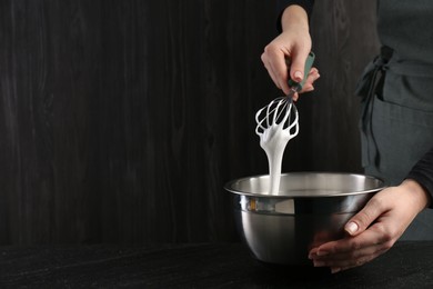 Woman making whipped cream with whisk at black table, closeup. Space for text