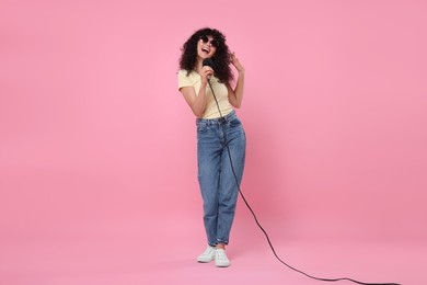 Photo of Beautiful young woman with microphone and sunglasses singing on pink background