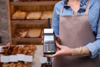 Woman holding payment terminal in bakery, closeup. Space for text