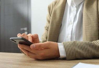 Photo of Woman using smartphone at wooden table indoors, closeup