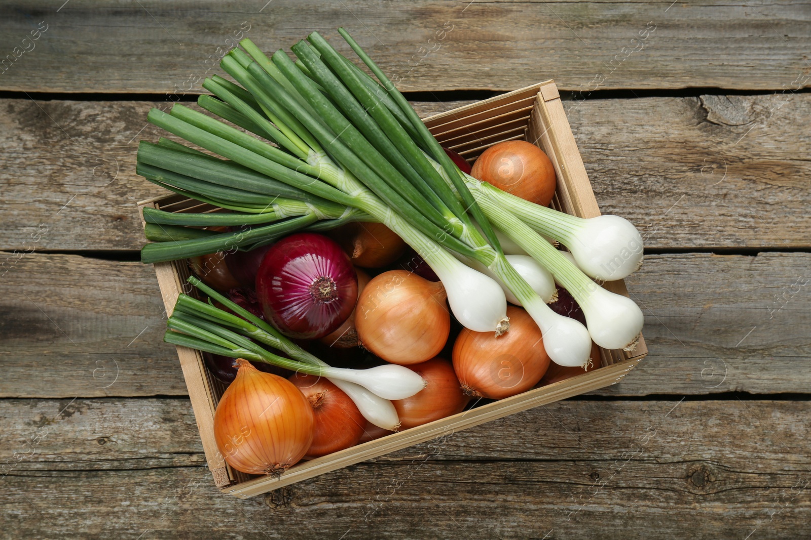 Photo of Crate with different kinds of onions on wooden table, top view