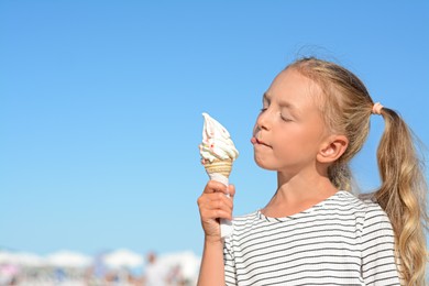 Photo of Adorable little girl with delicious ice cream against blue sky, space for text