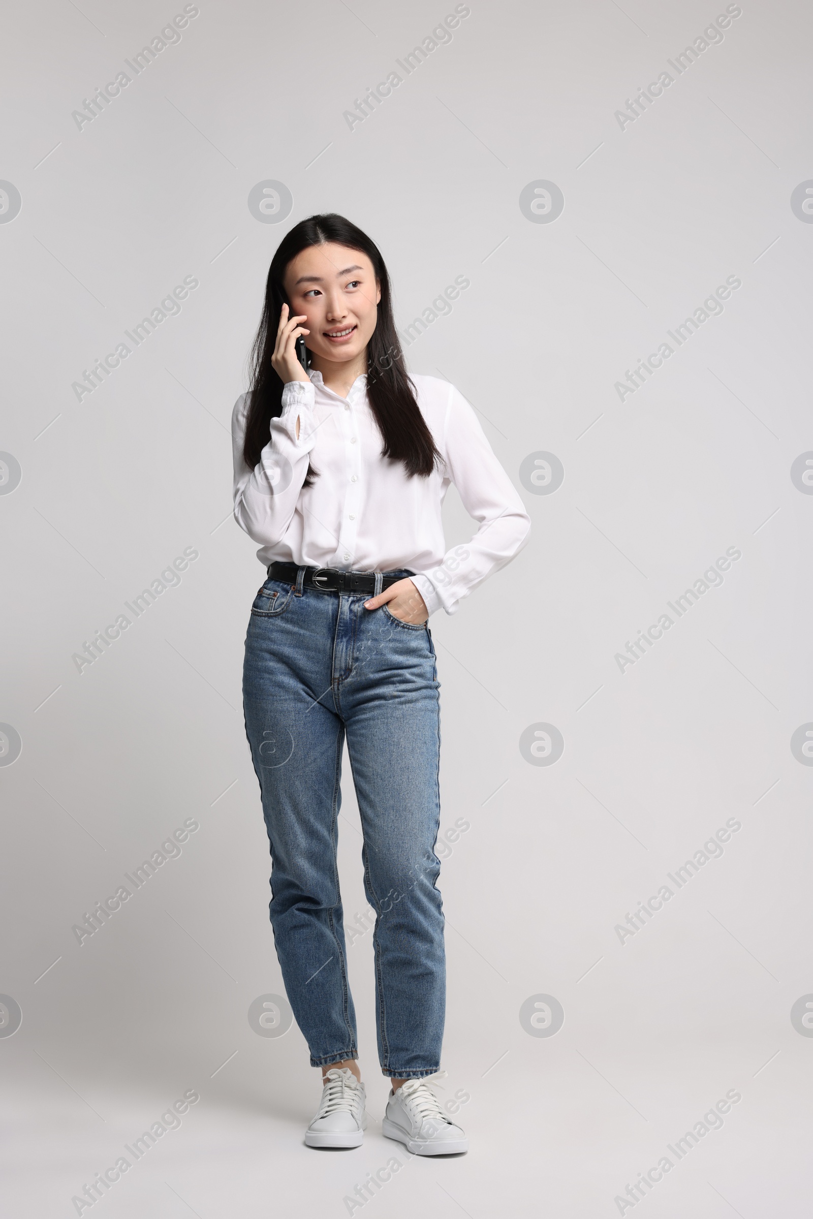 Photo of Full length portrait of smiling woman talking by smartphone on light background