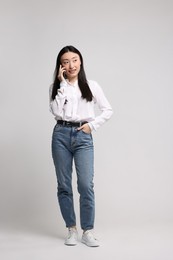 Photo of Full length portrait of smiling woman talking by smartphone on light background