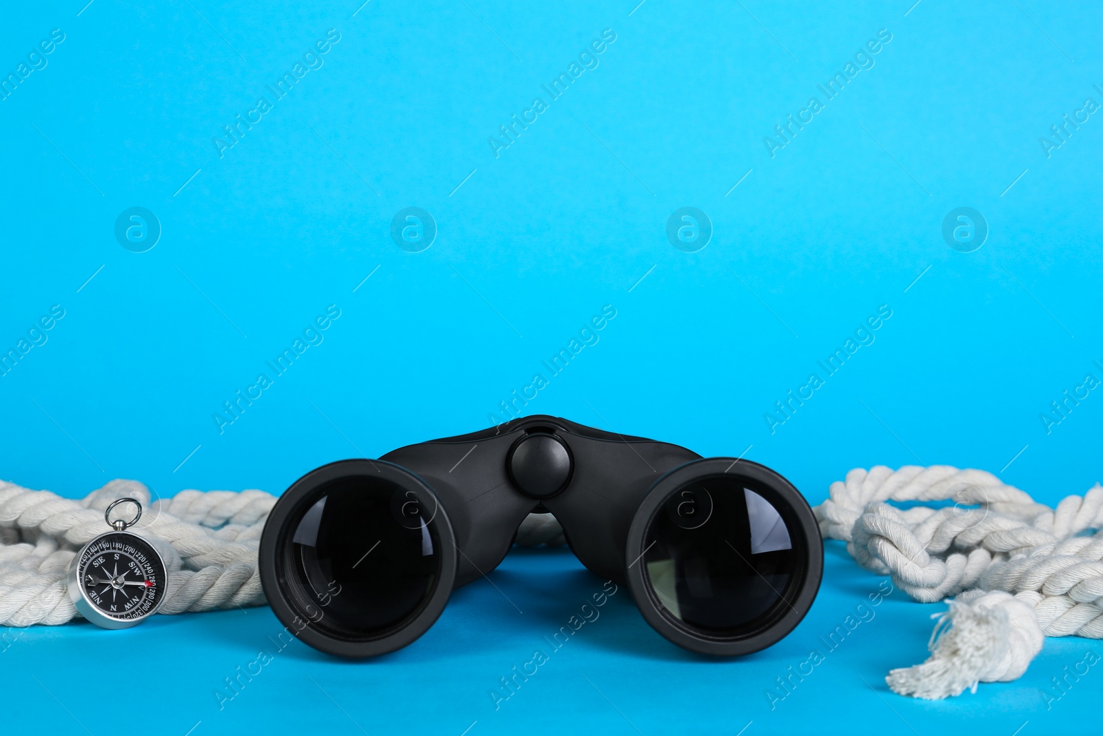 Photo of Modern binoculars, compass and rope on light blue background, space for text