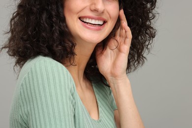 Young woman using teeth whitening strip on grey background, closeup. Space for text