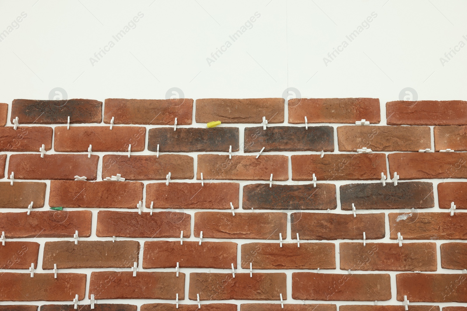 Photo of Decorative bricks with tile leveling system on white wall