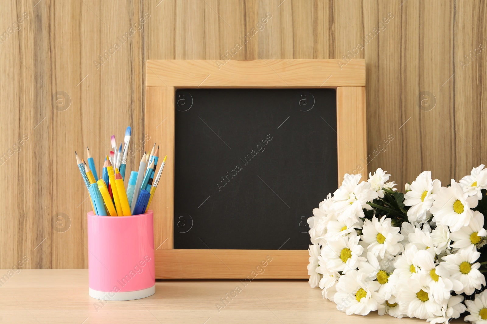 Photo of Blackboard, stationery and flowers on table near wooden wall, space for text. Teacher's Day