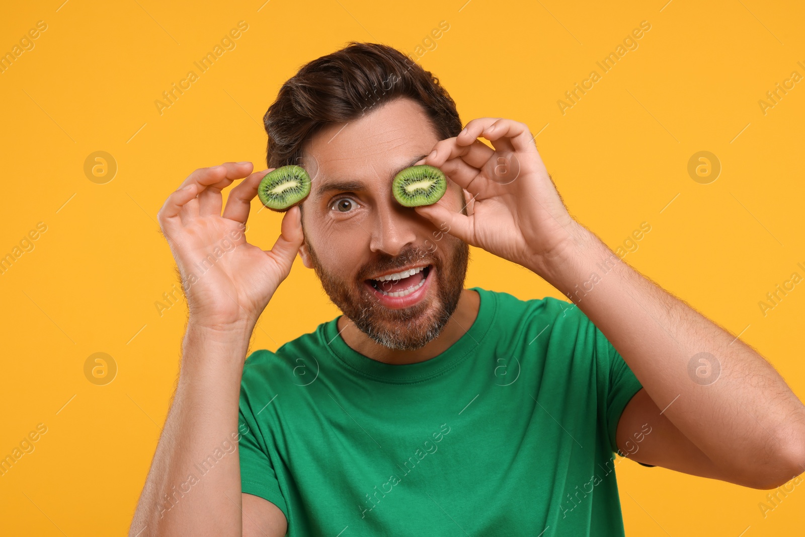 Photo of Emotional man holding halves of kiwi on orange background
